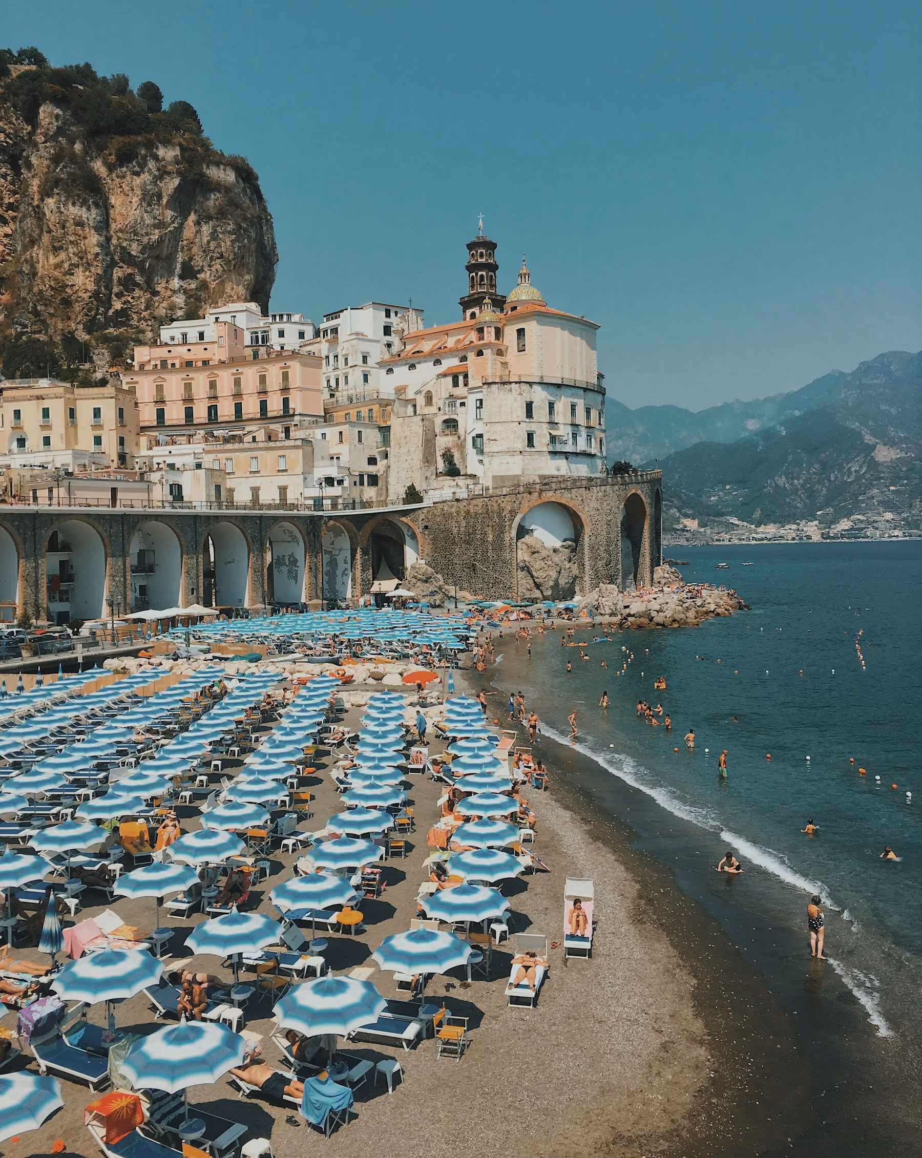 Rows of blue and white umbrellas on the beach at Atrani below the town's arches in summer