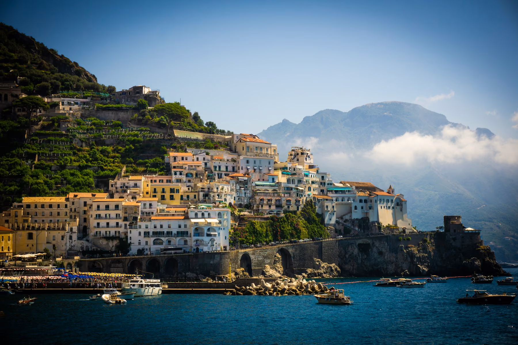 Pastel houses and a harbour wall on the Amalfi Coast, with cloud over the mountains