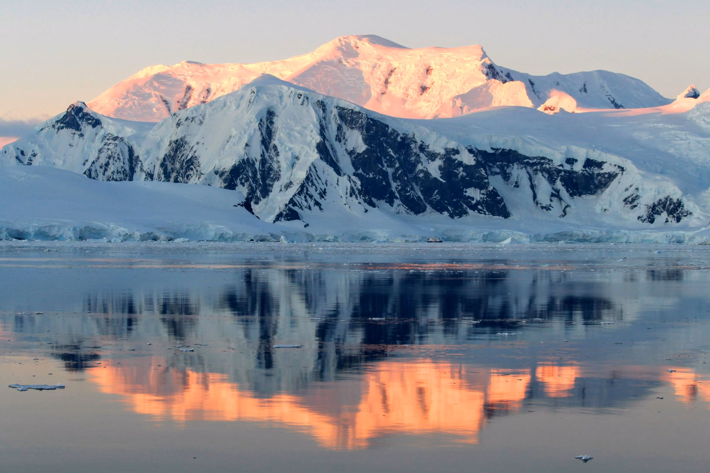 Antarctic peaks lit pink at sunset, reflected in still water