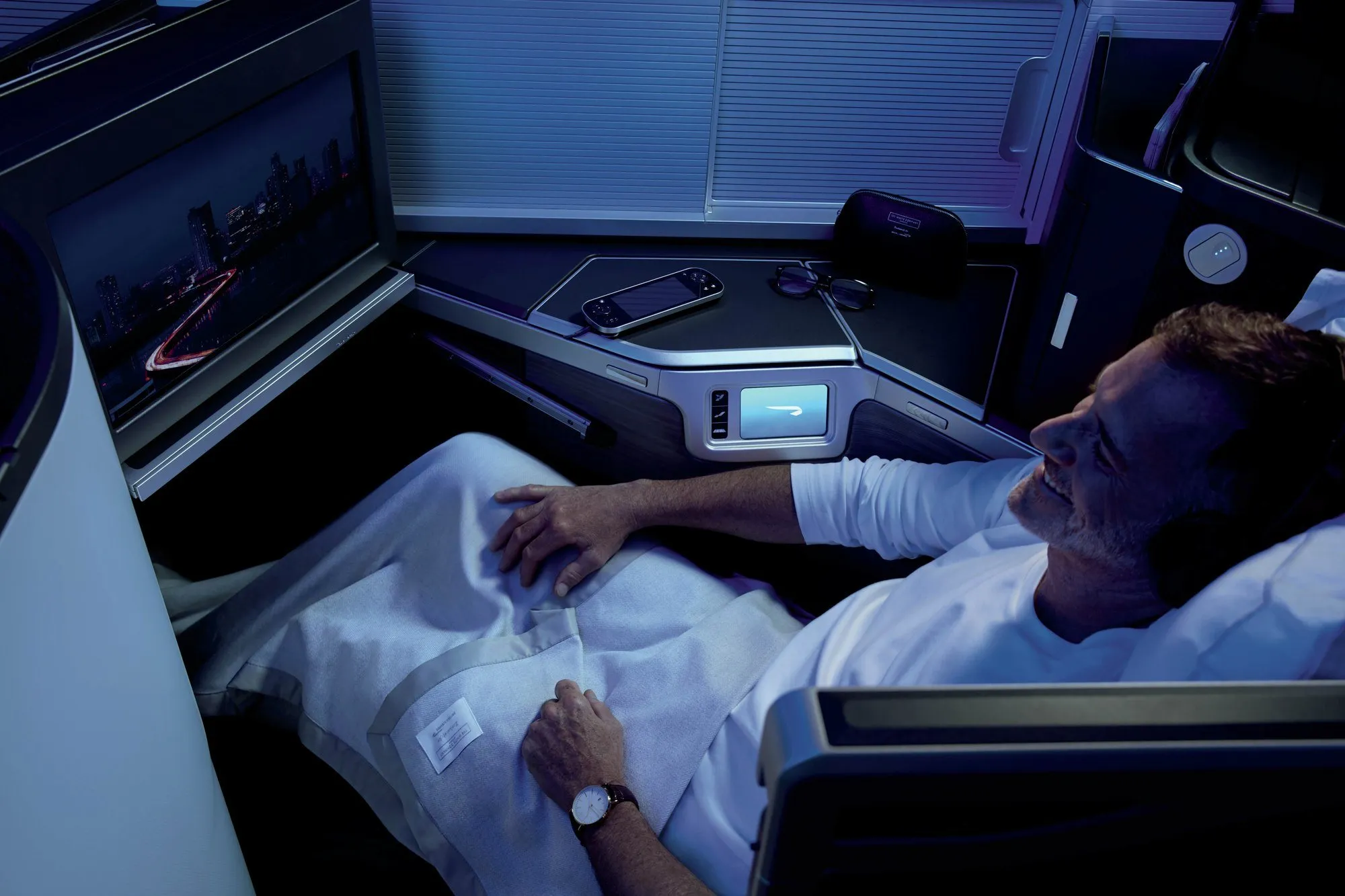 A passenger lying flat in a Club Suite at night, under a blanket