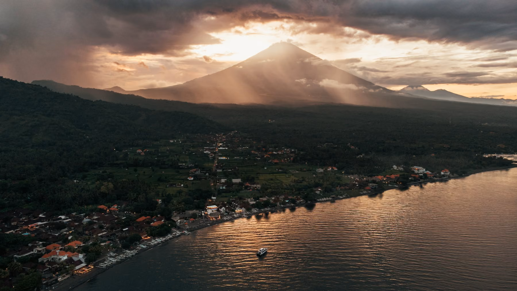 Sunset rays over Mount Agung, seen from the air above the Amed coastline and a lone boat