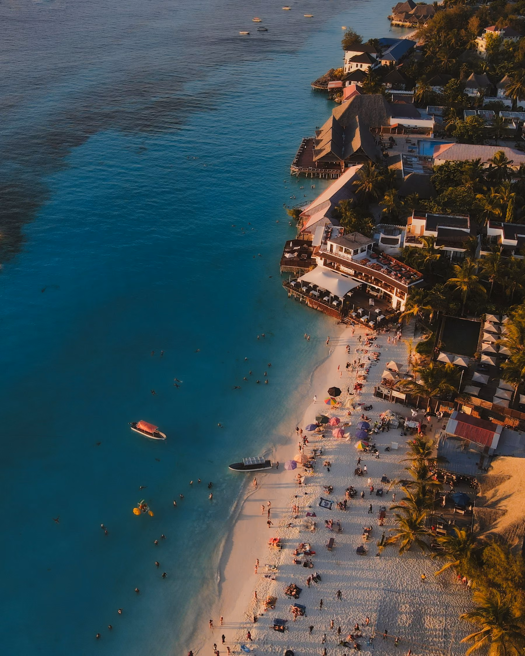 Aerial view of a busy west coast beach in Barbados, turquoise water meeting a line of beachfront hotels
