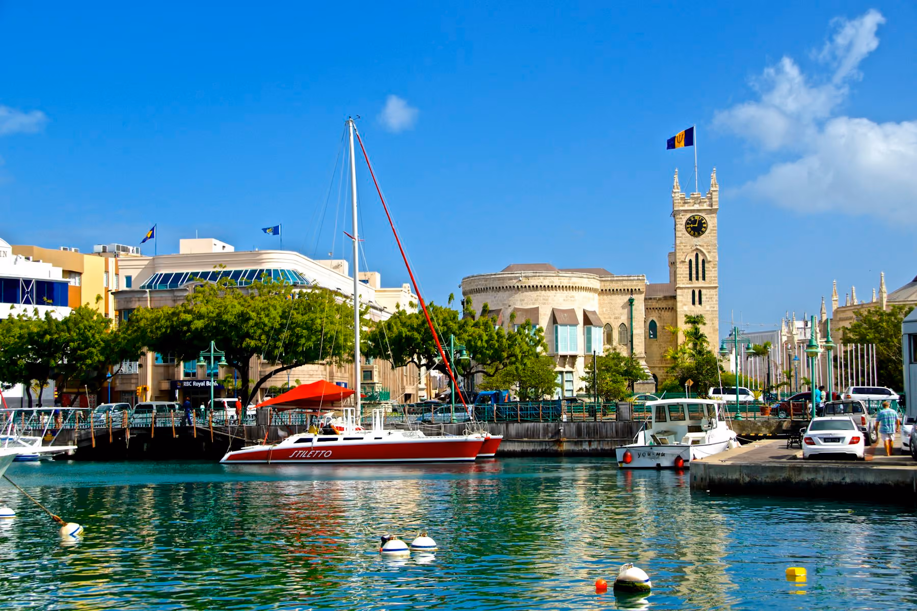 The Careenage in Bridgetown with moored boats and the Parliament Buildings clock tower under a blue sky
