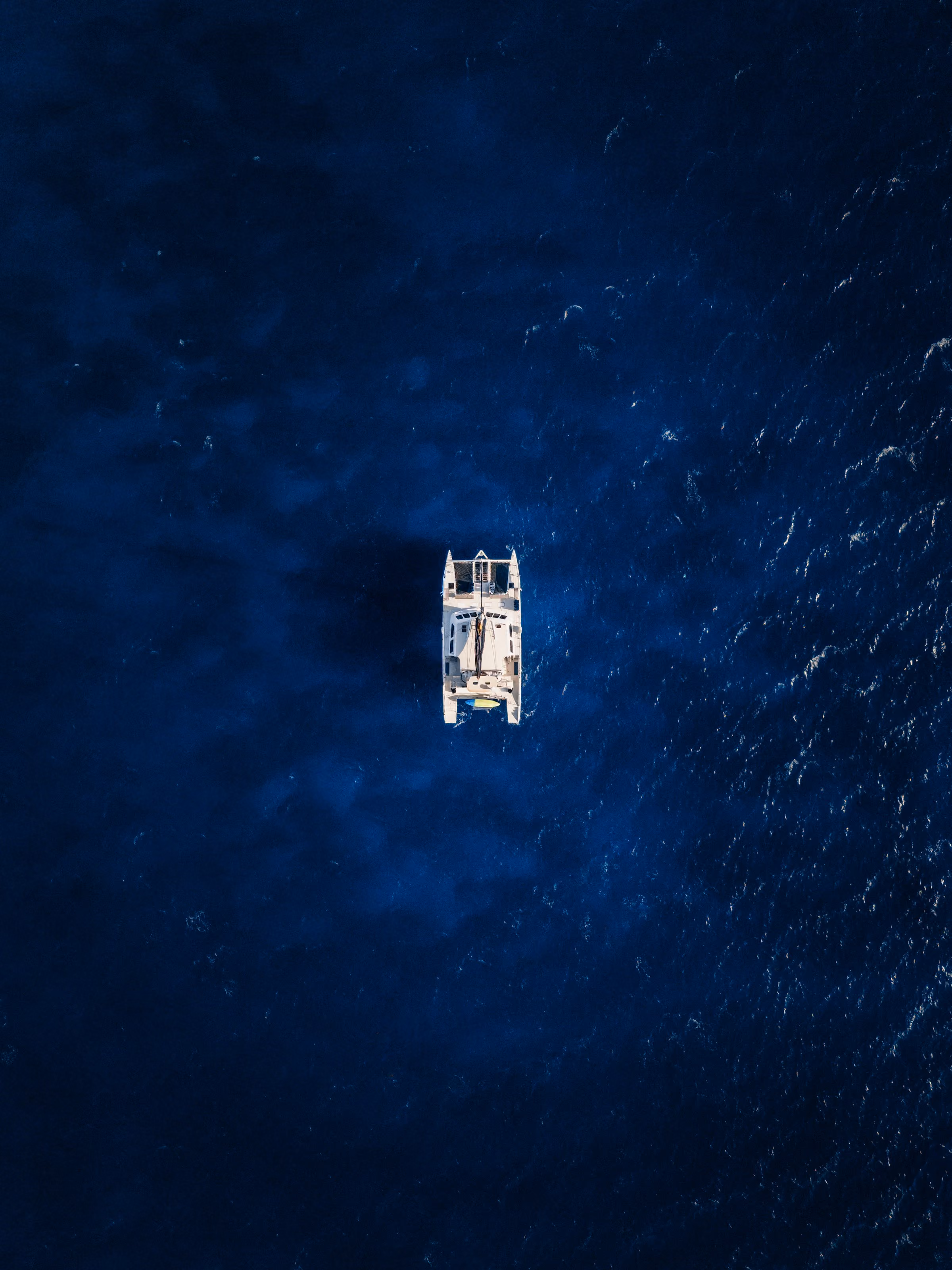 A sailing catamaran from above, alone on deep blue water