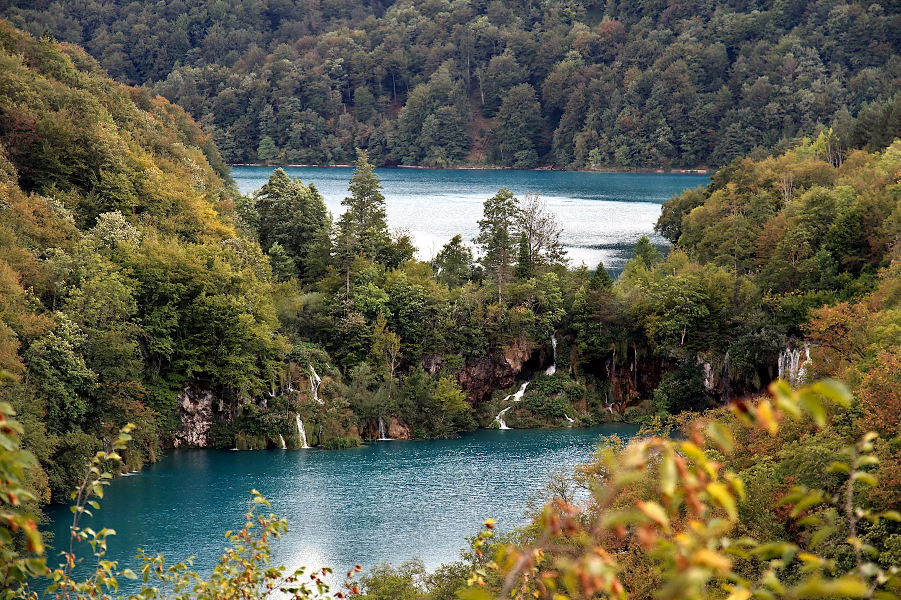 Lakes and waterfalls at Plitvice framed by forest, with leaves beginning to turn in autumn