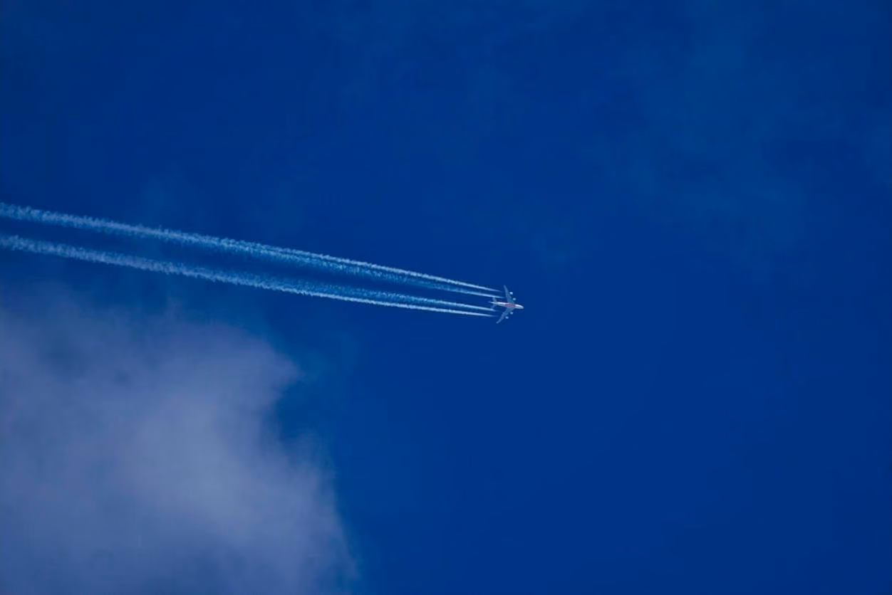 An Emirates A380 at cruising height, four contrails behind it across a deep blue sky
