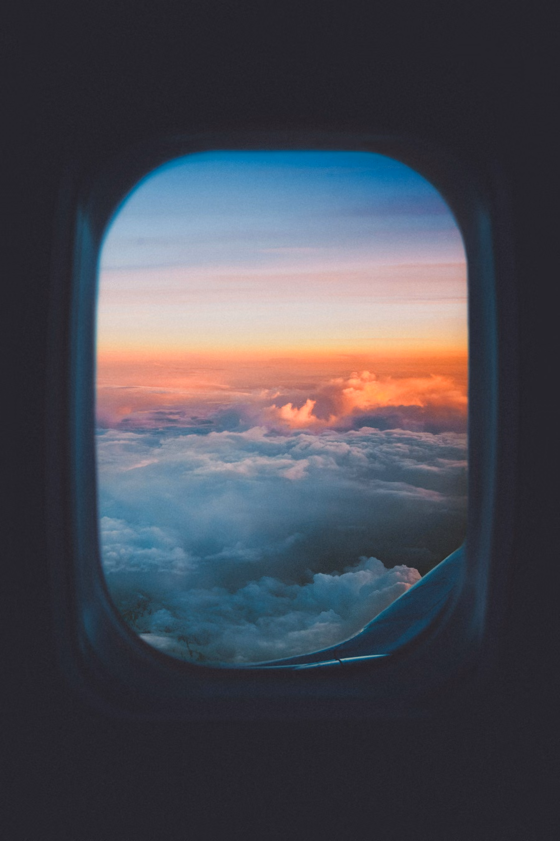 An aircraft window looking out over a sea of clouds at sunset