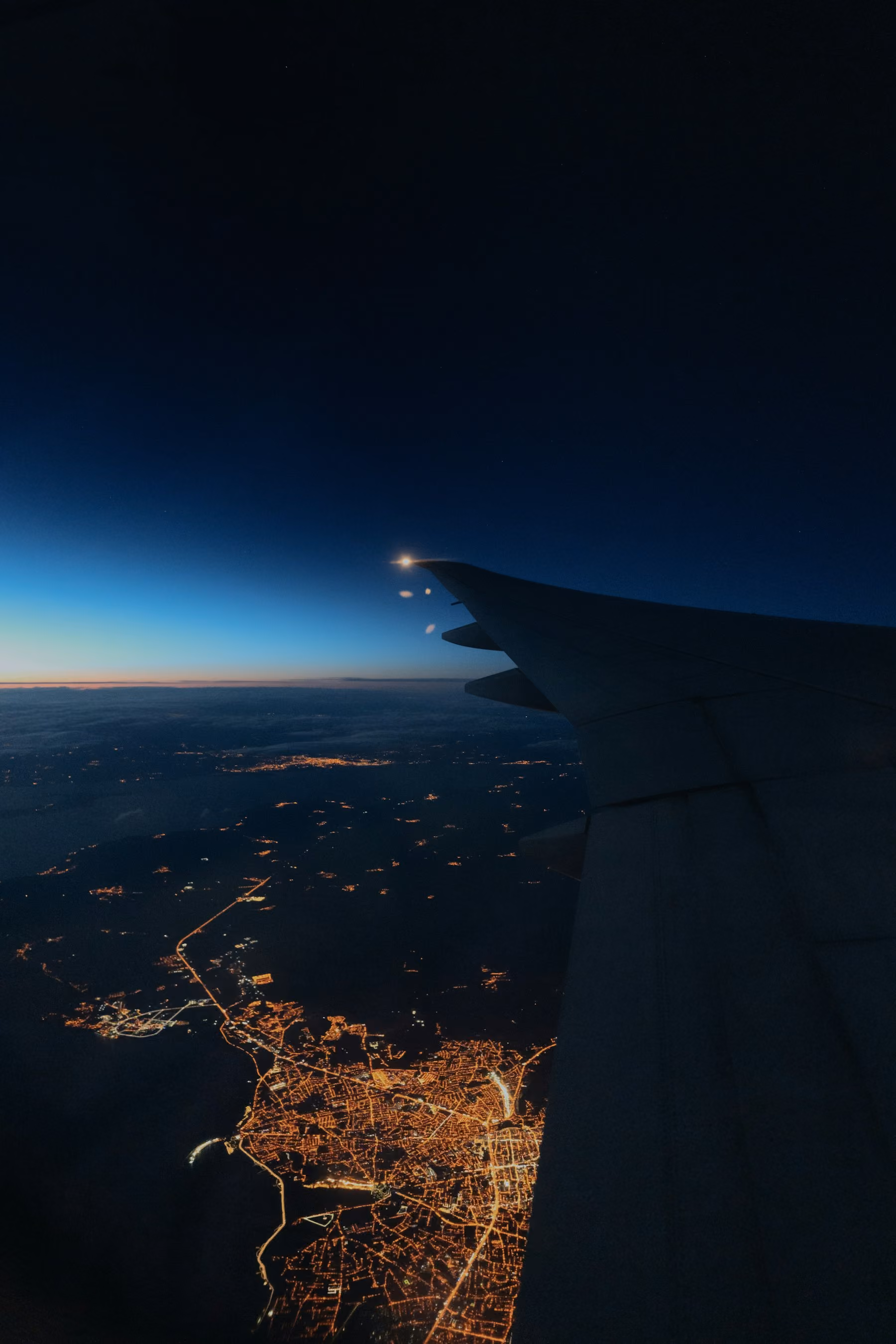 City lights spreading below an aircraft wing at night
