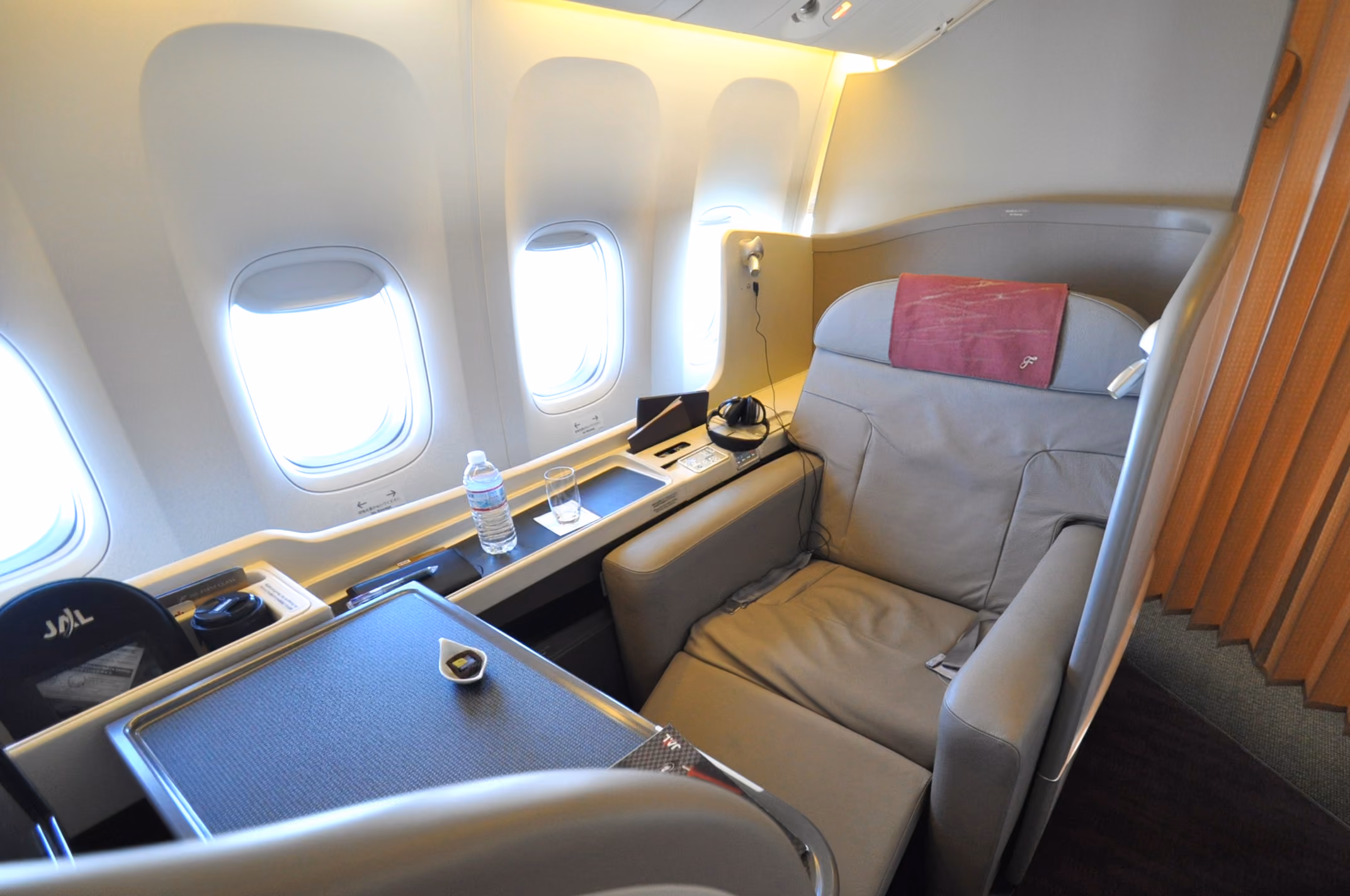 An enclosed first class suite with a dining table, water bottle and glass, seen beside two cabin windows
