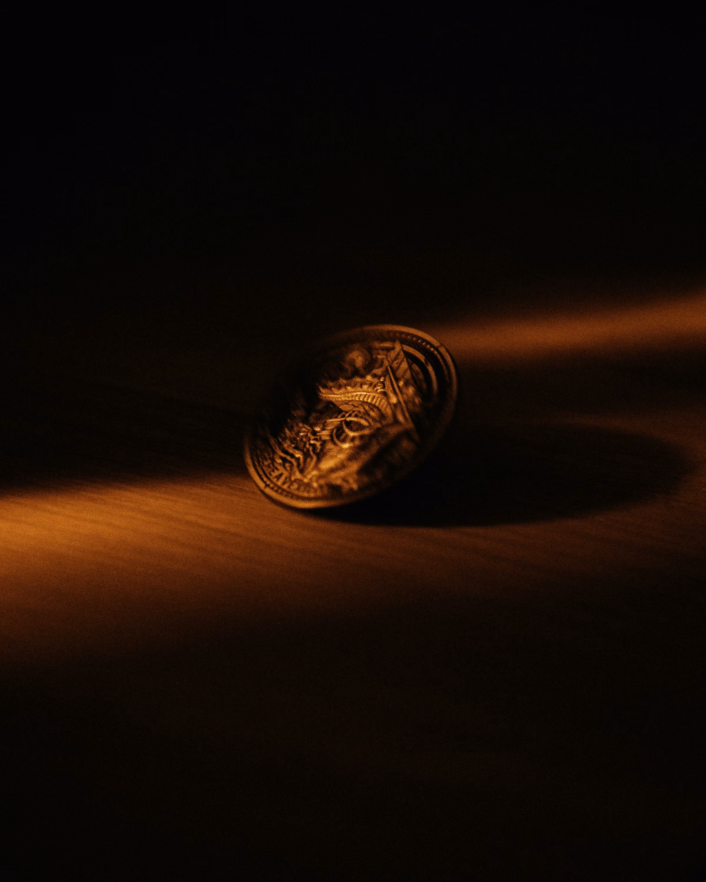 A single gold coin catching the light on a dark surface