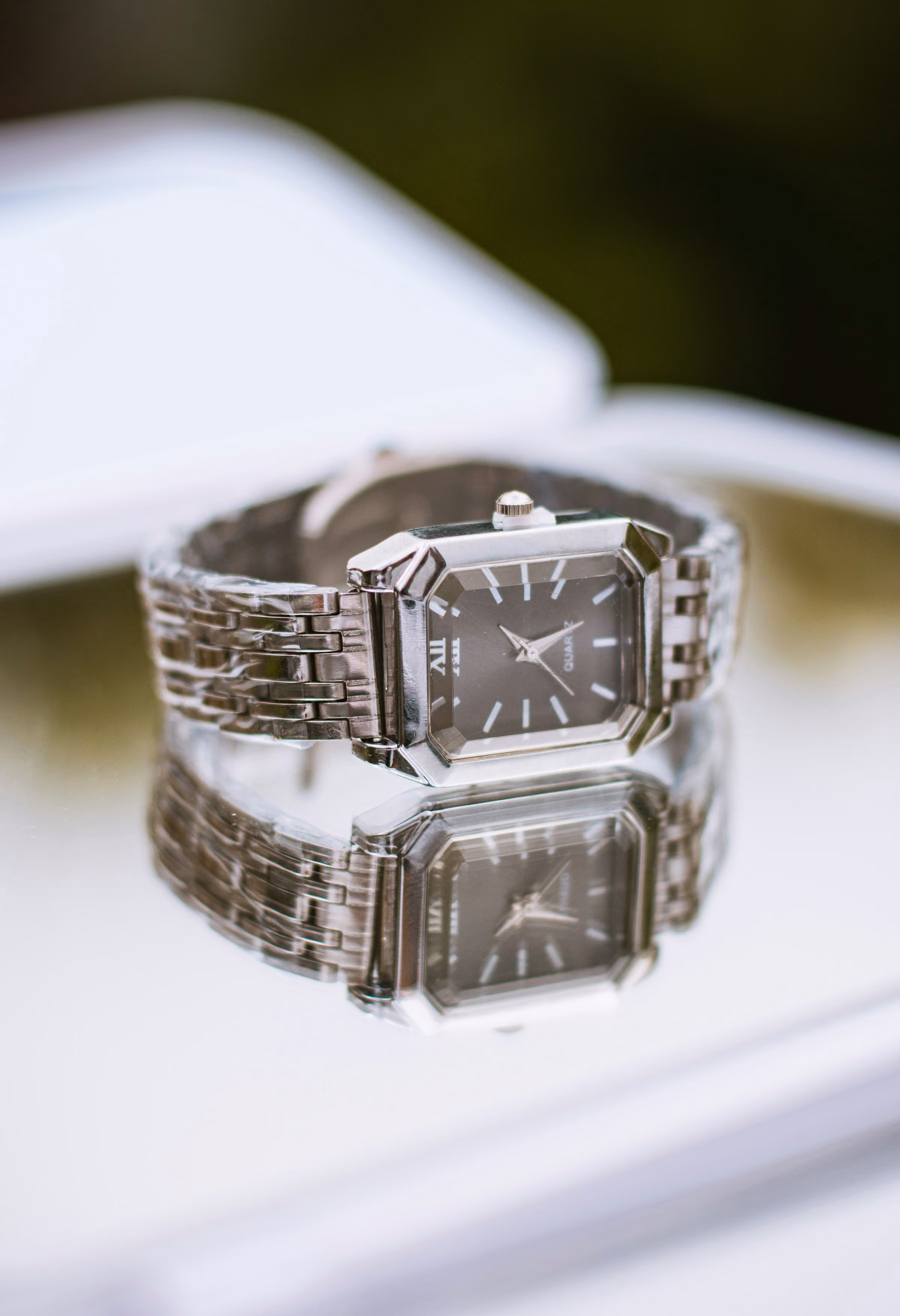 A steel rectangular watch reflected on a glossy surface