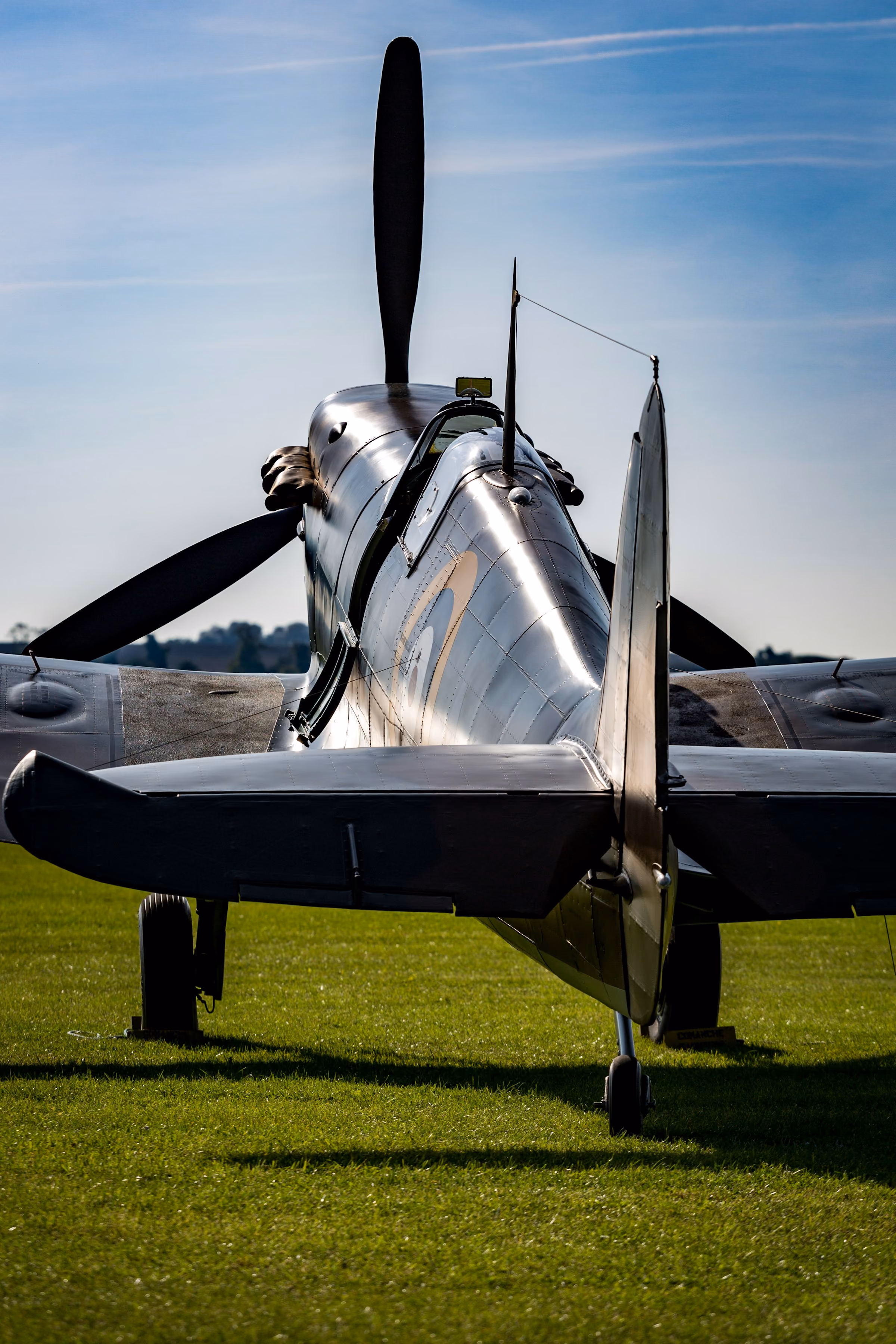 A silver Spitfire on the grass, seen from behind