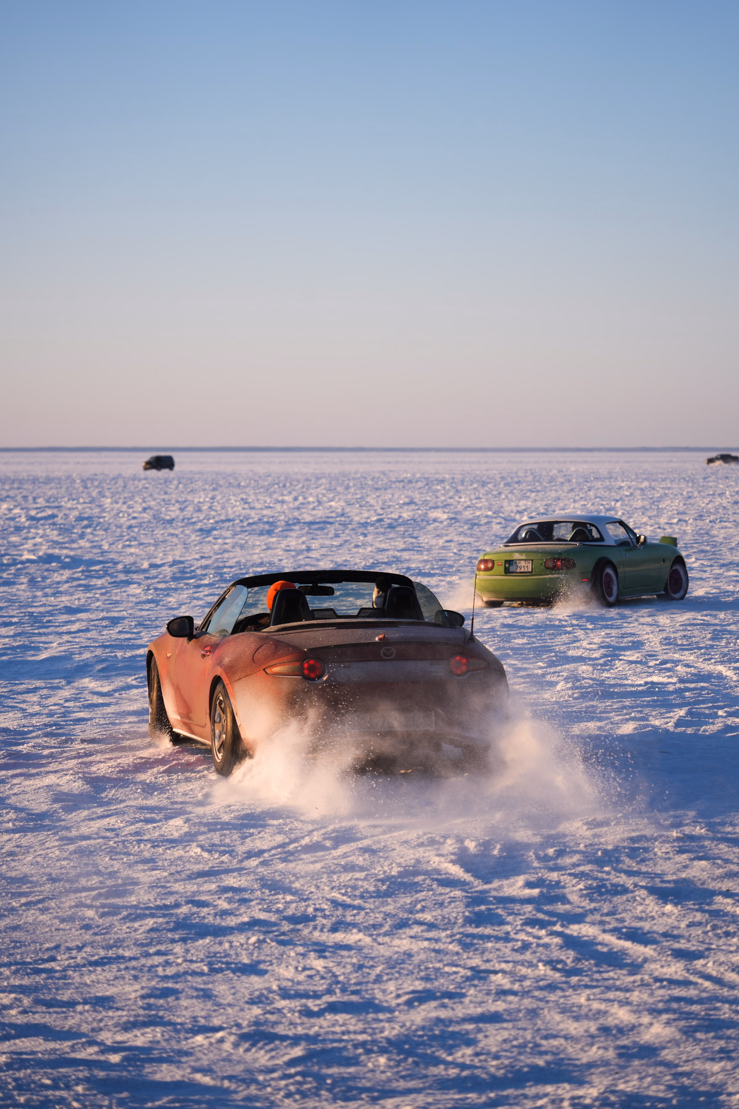 A red sports car throwing up snow on an ice track