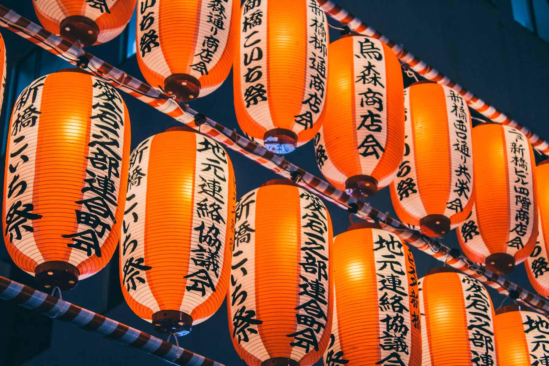 Rows of glowing paper lanterns strung above a Tokyo street during a summer festival