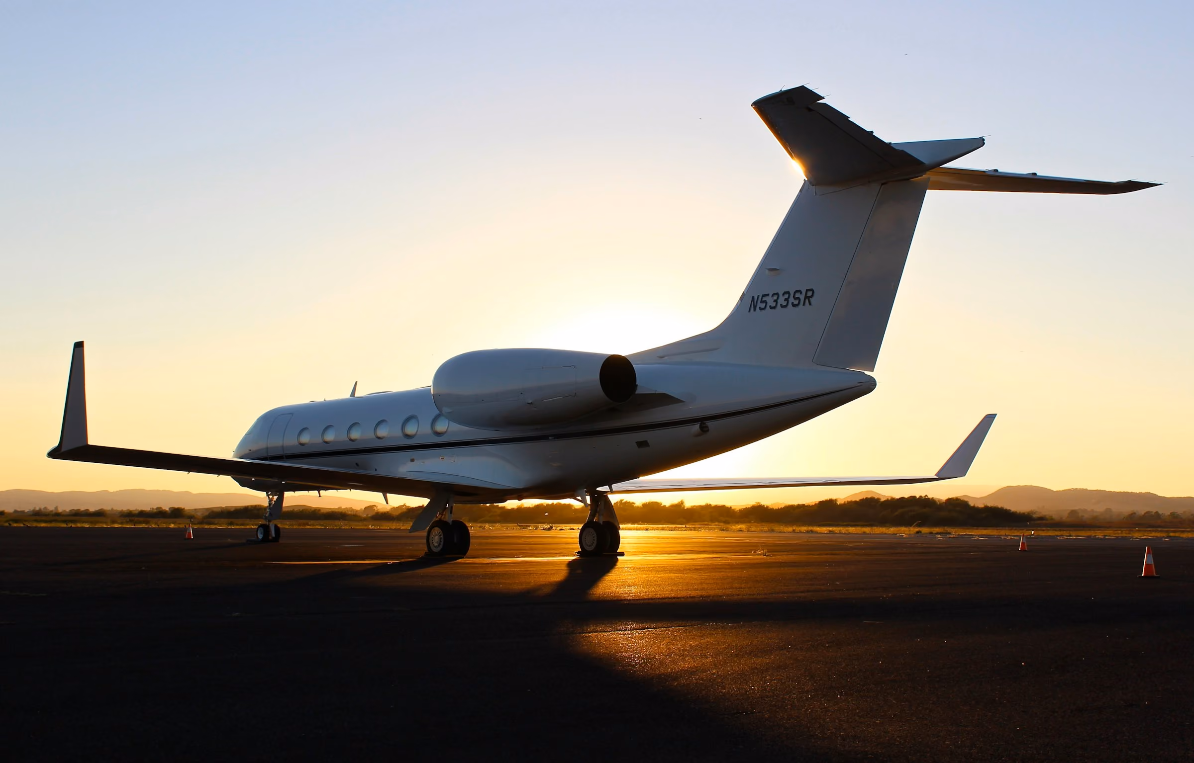 A private jet charter aircraft on the tarmac at sunset, the sky gold behind it