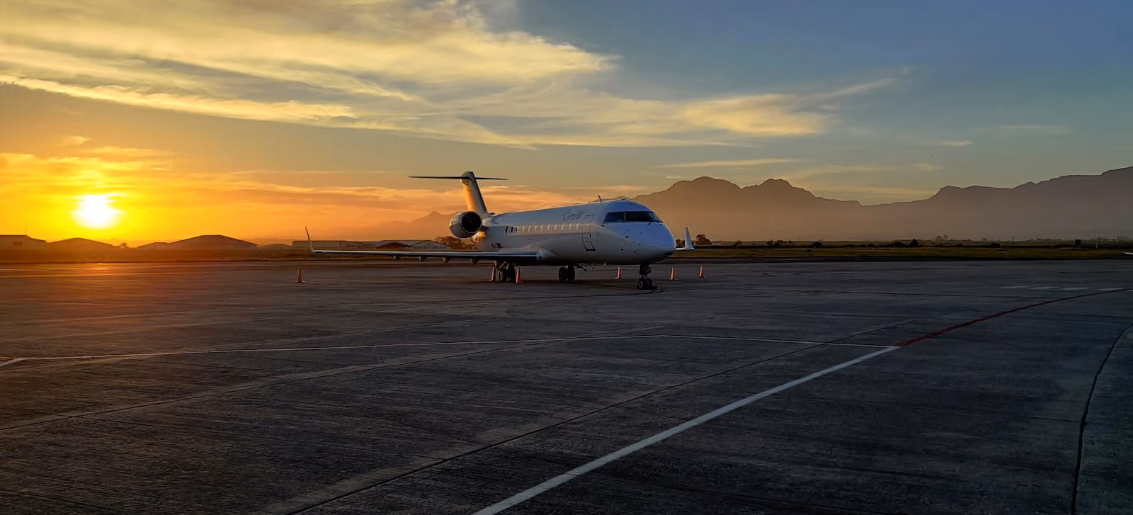 A small private jet on the apron at sunset, mountains on the horizon