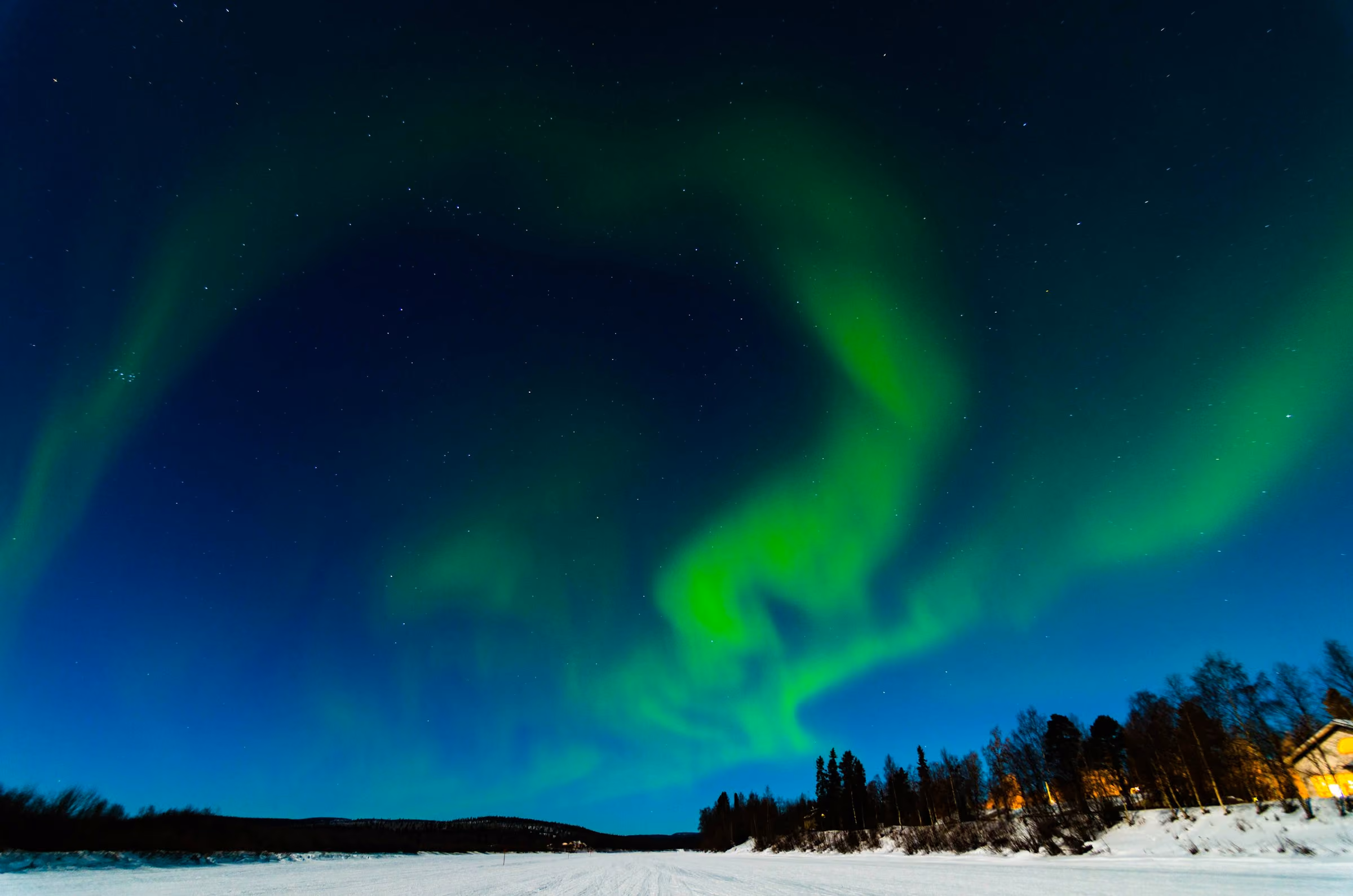 Lapland holidays: the northern lights over a snowy forest and a lit cabin