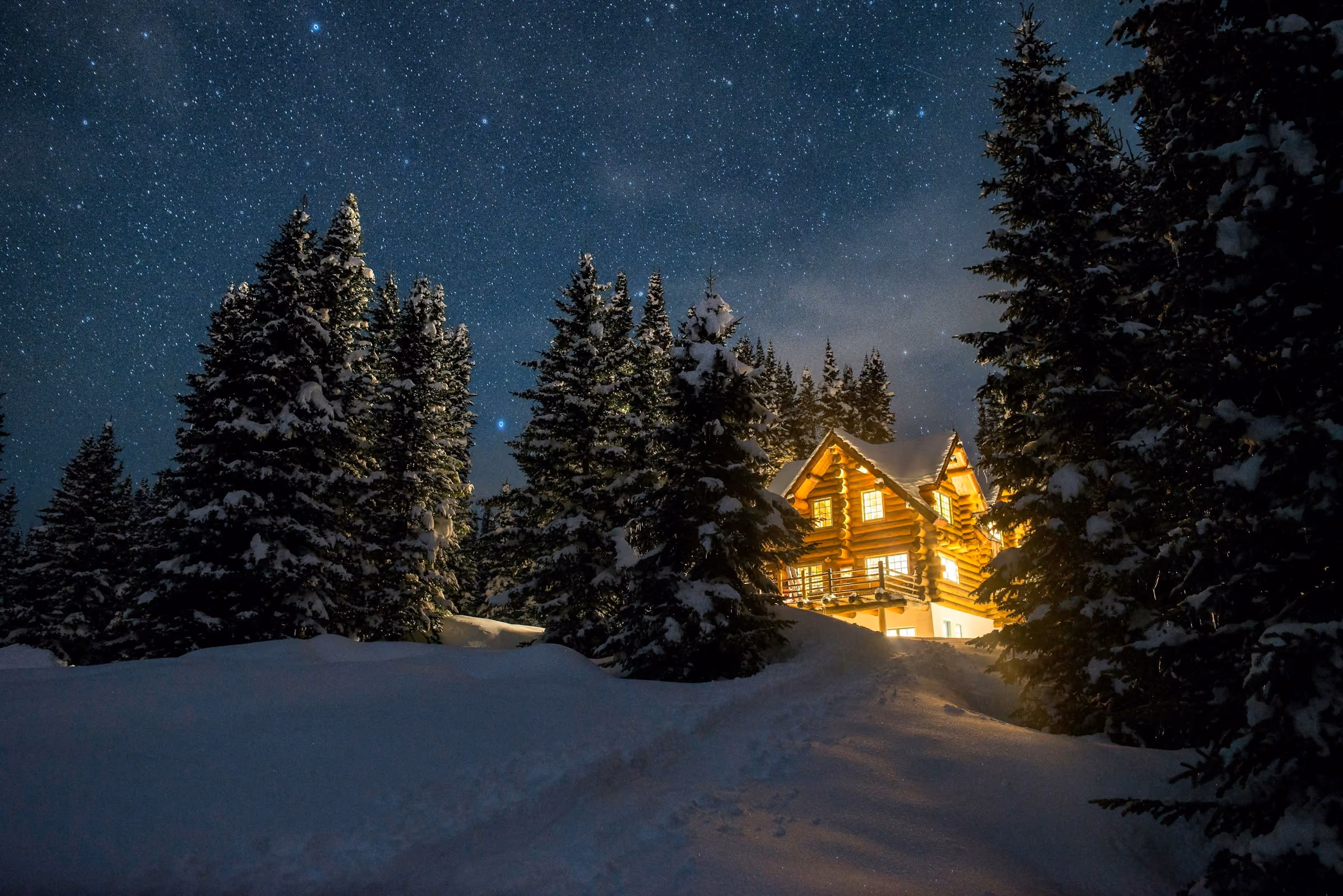A lit wooden lodge among snow-covered pines under a starry sky