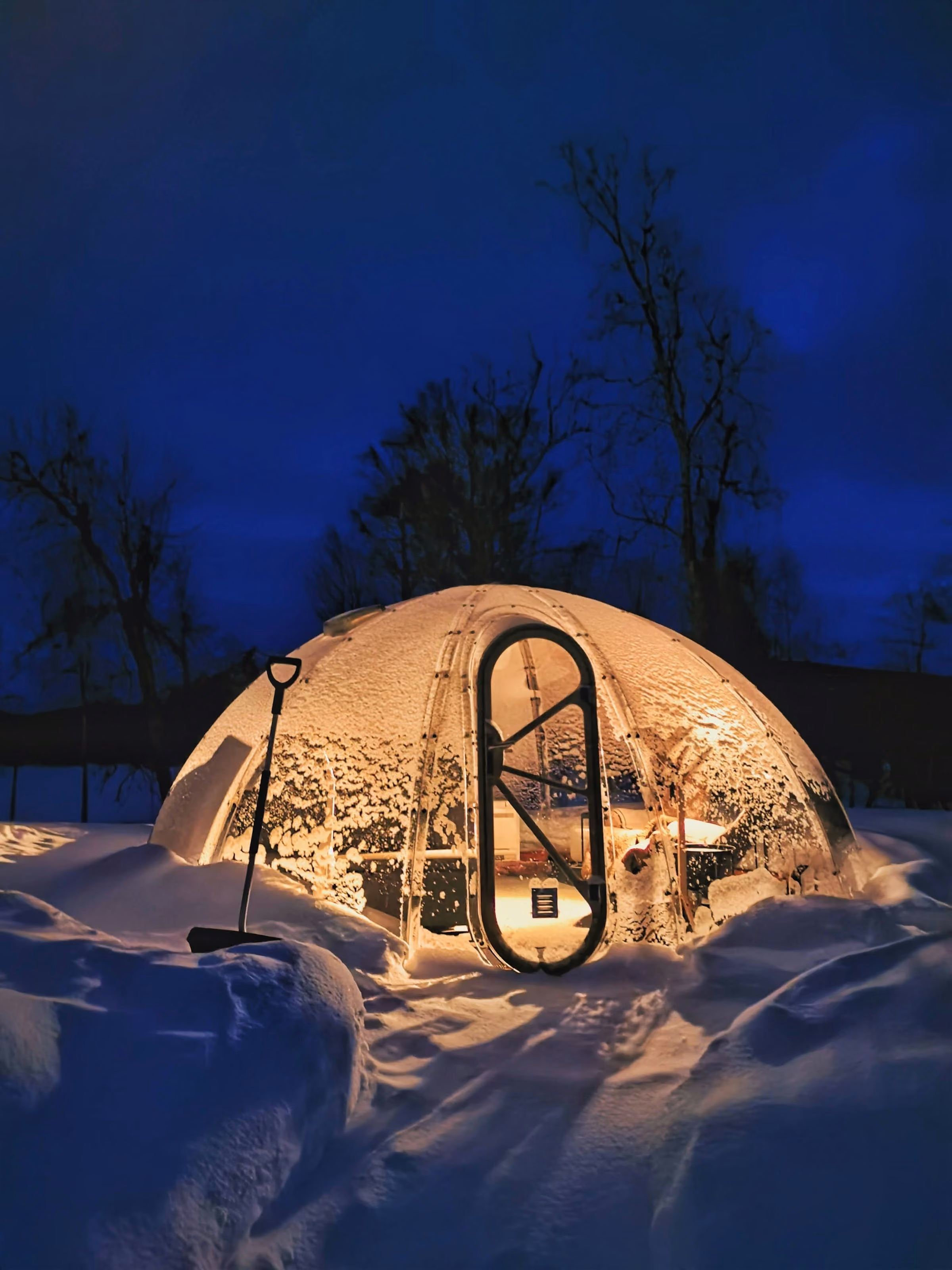 A glowing glass dome in the snow at night, the kind of room at Kakslauttanen