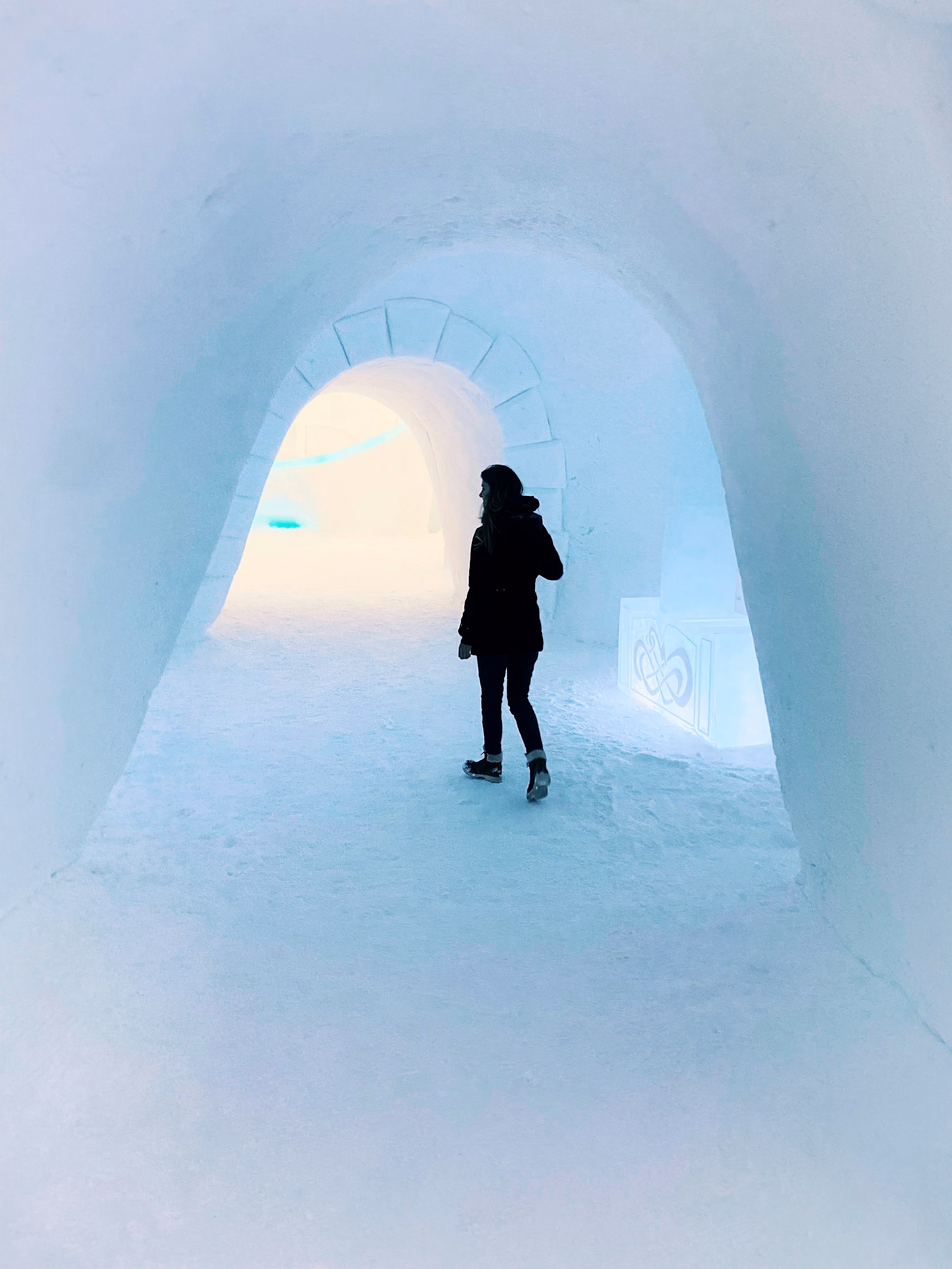 A person walking through a tunnel of ice and snow towards the light