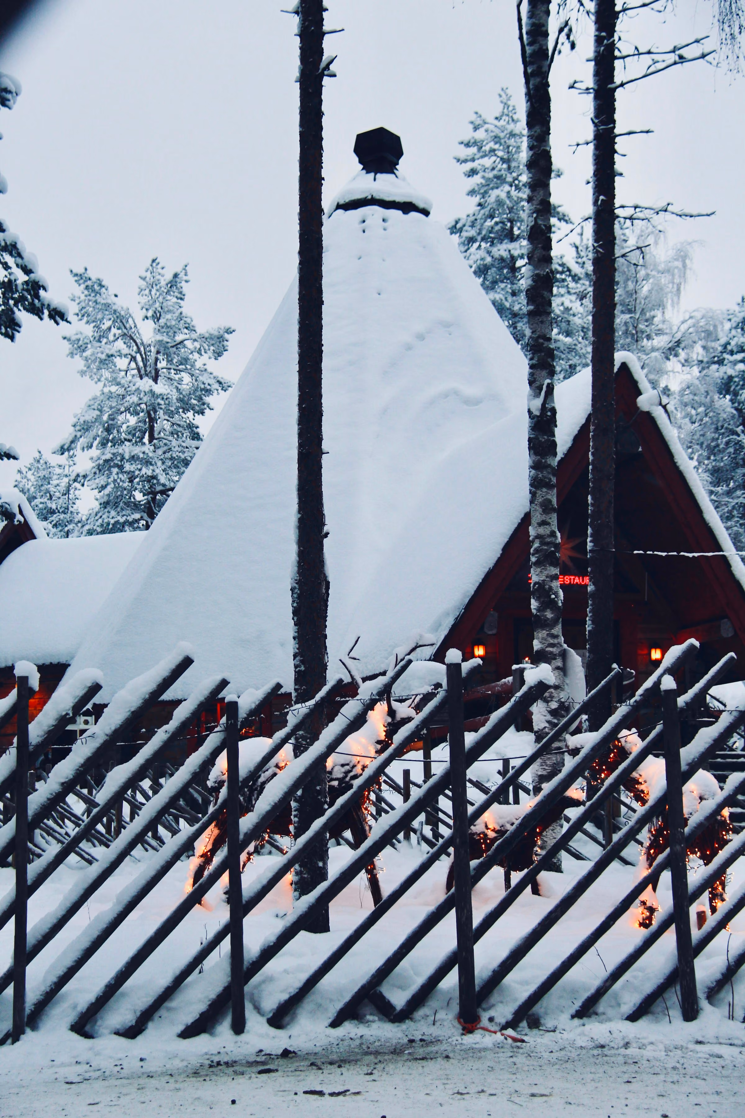 A snow-covered wooden kota hut behind a snowy fence
