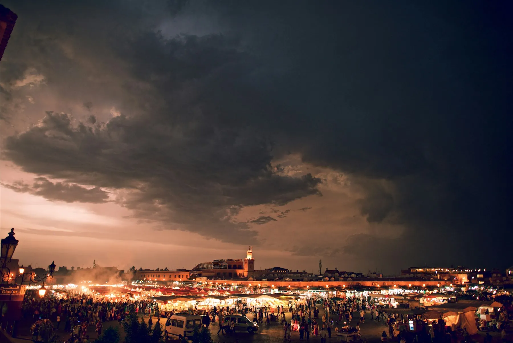 Storm clouds over the lit food stalls of Jemaa el-Fnaa at dusk, the best time to visit Morocco's Marrakech