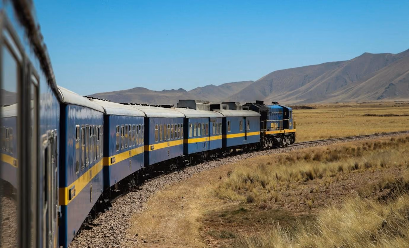 A blue and yellow train curving across the golden Peruvian altiplano