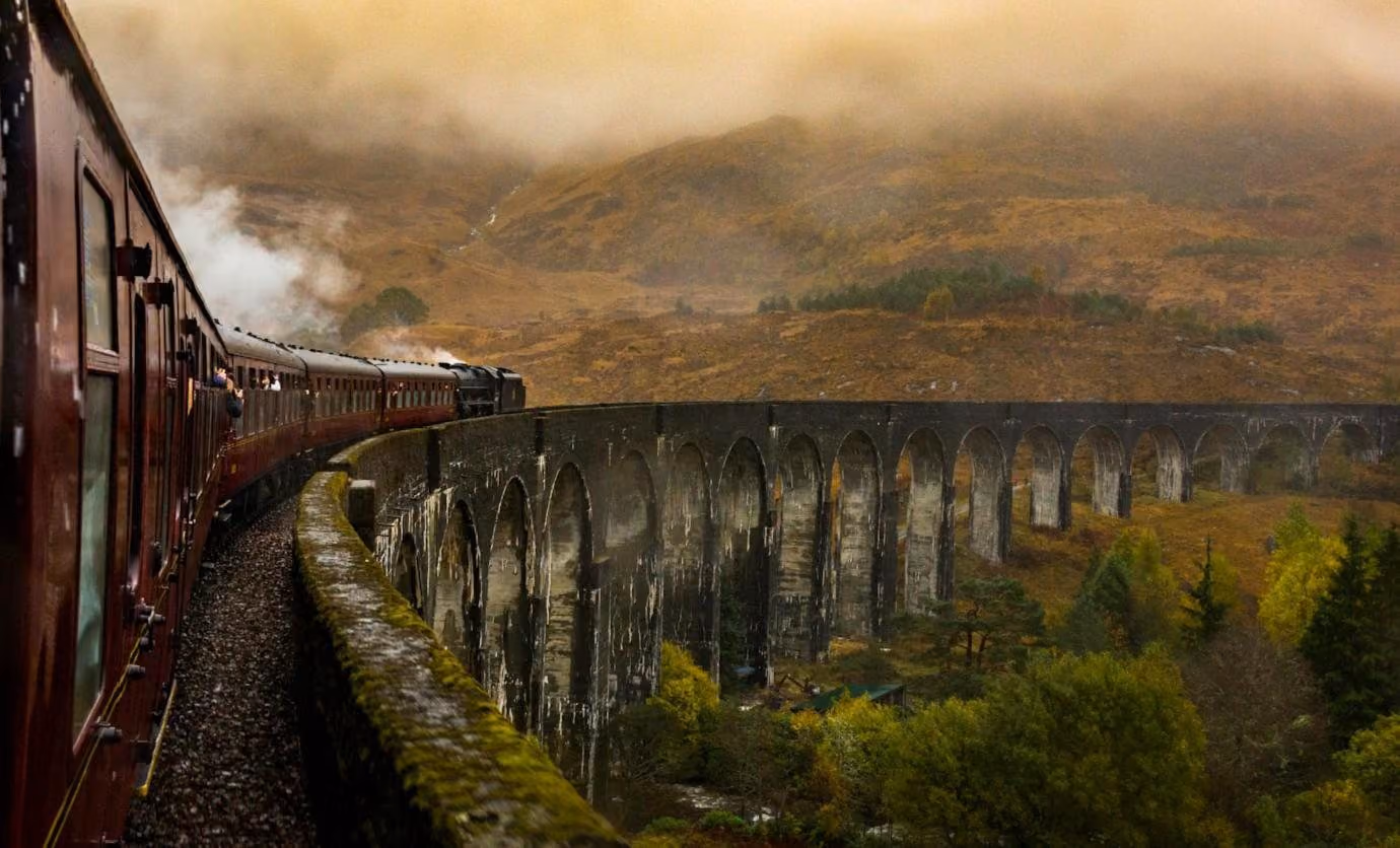 A train crossing a stone viaduct in the Scottish Highlands, autumn mist on the hills