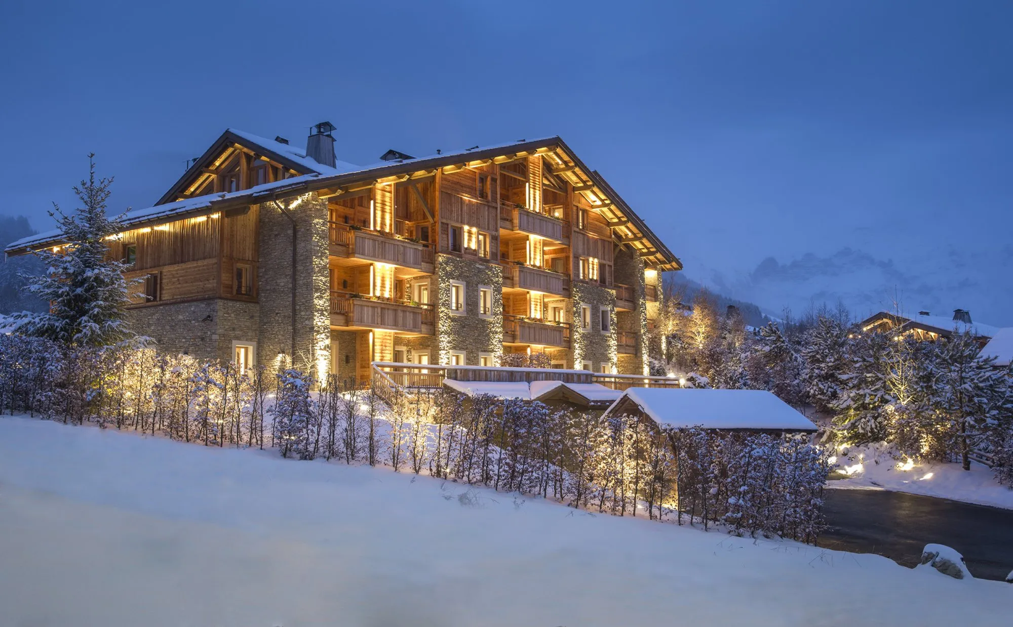 Four Seasons Megève lit up on a winter evening, its stone and timber chalets under snow