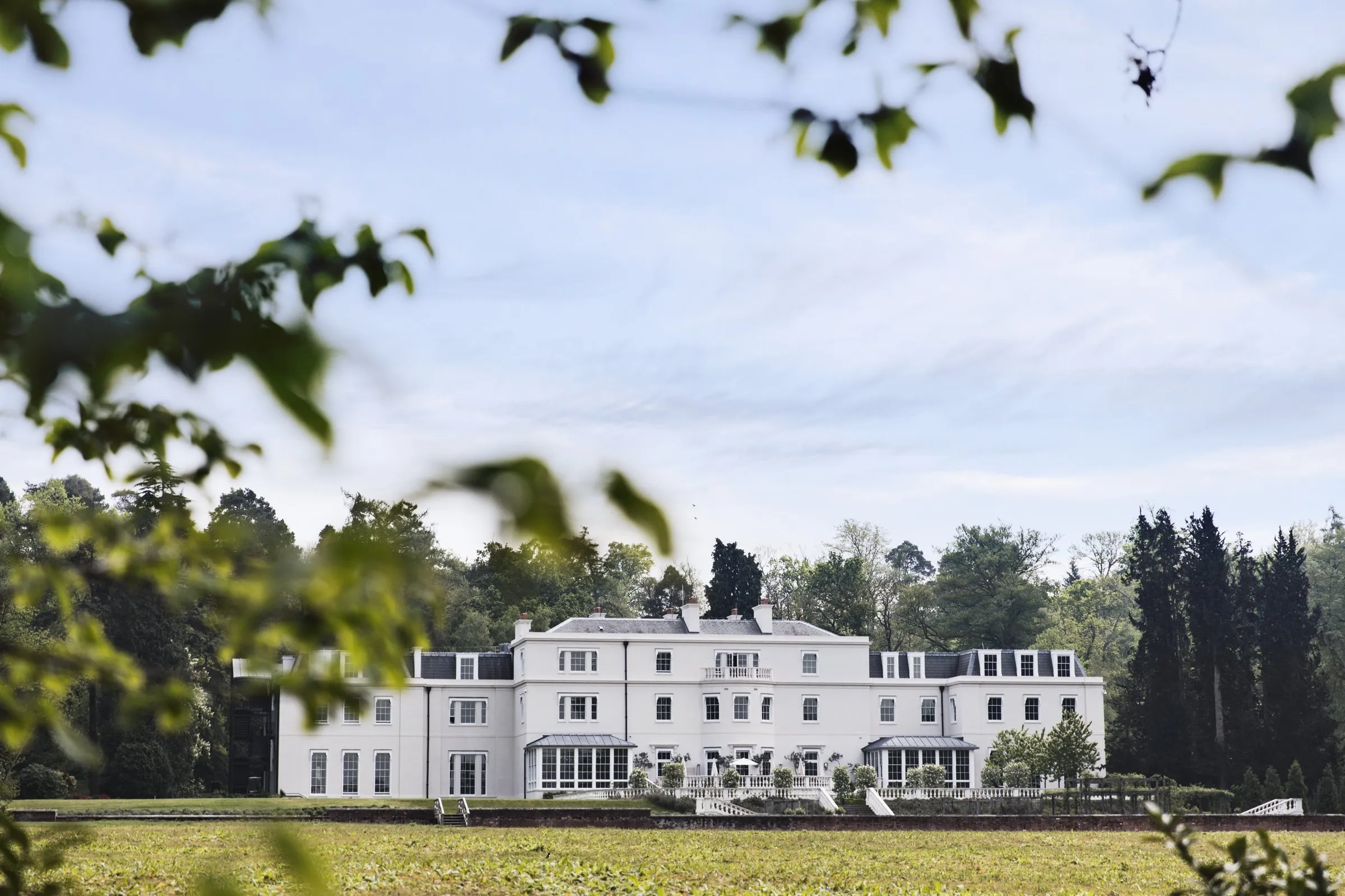 The white mansion house at Coworth Park beyond the trees