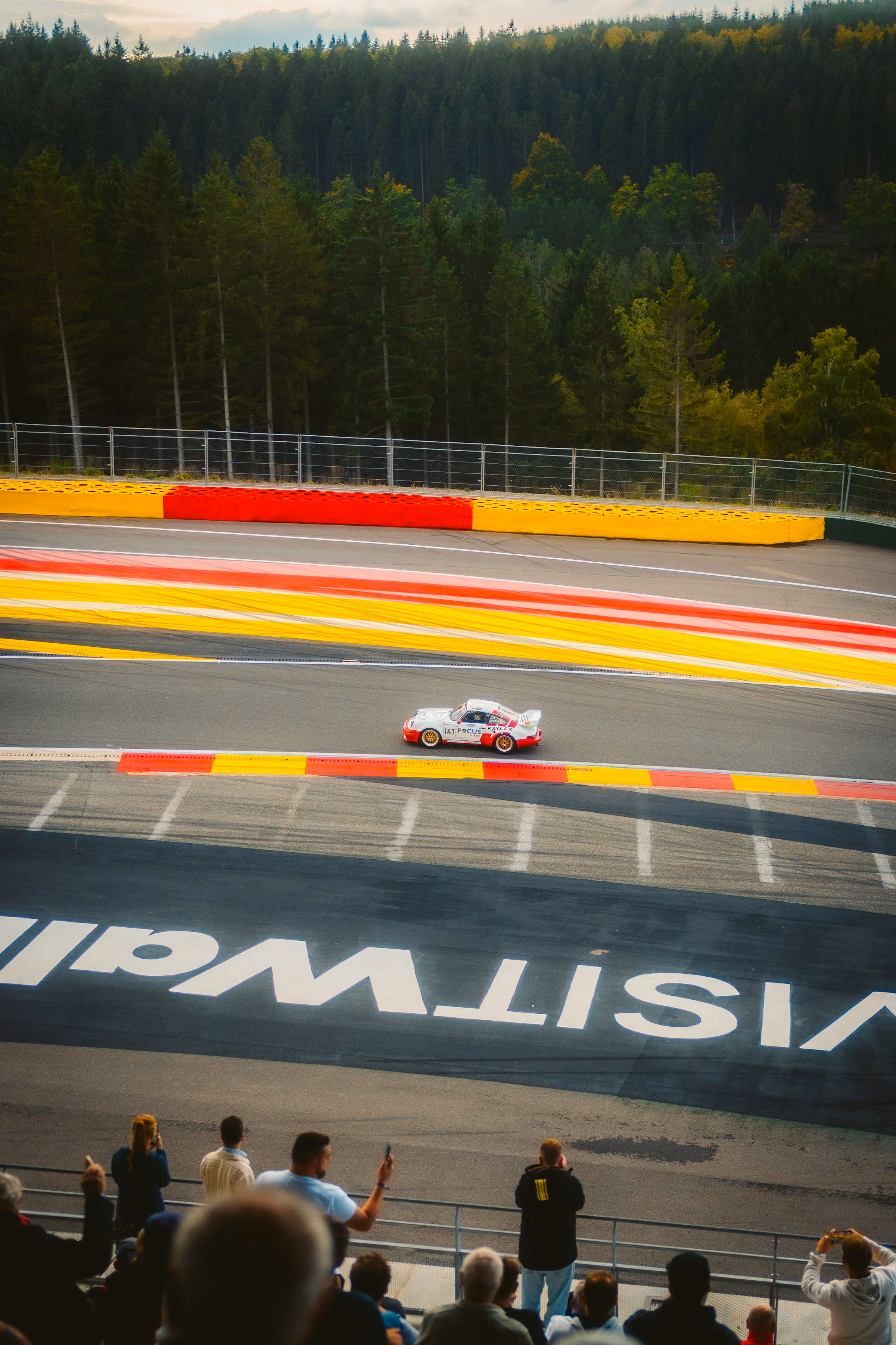 A Porsche racing past the red and yellow kerbs at Spa-Francorchamps