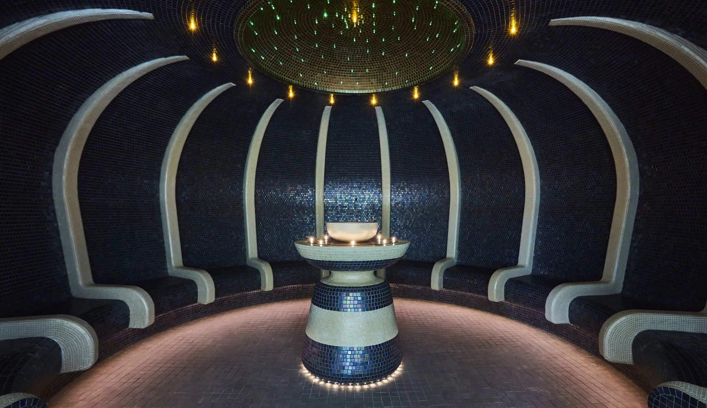 A domed thermal room lined with dark mosaic and lit by tiny stars