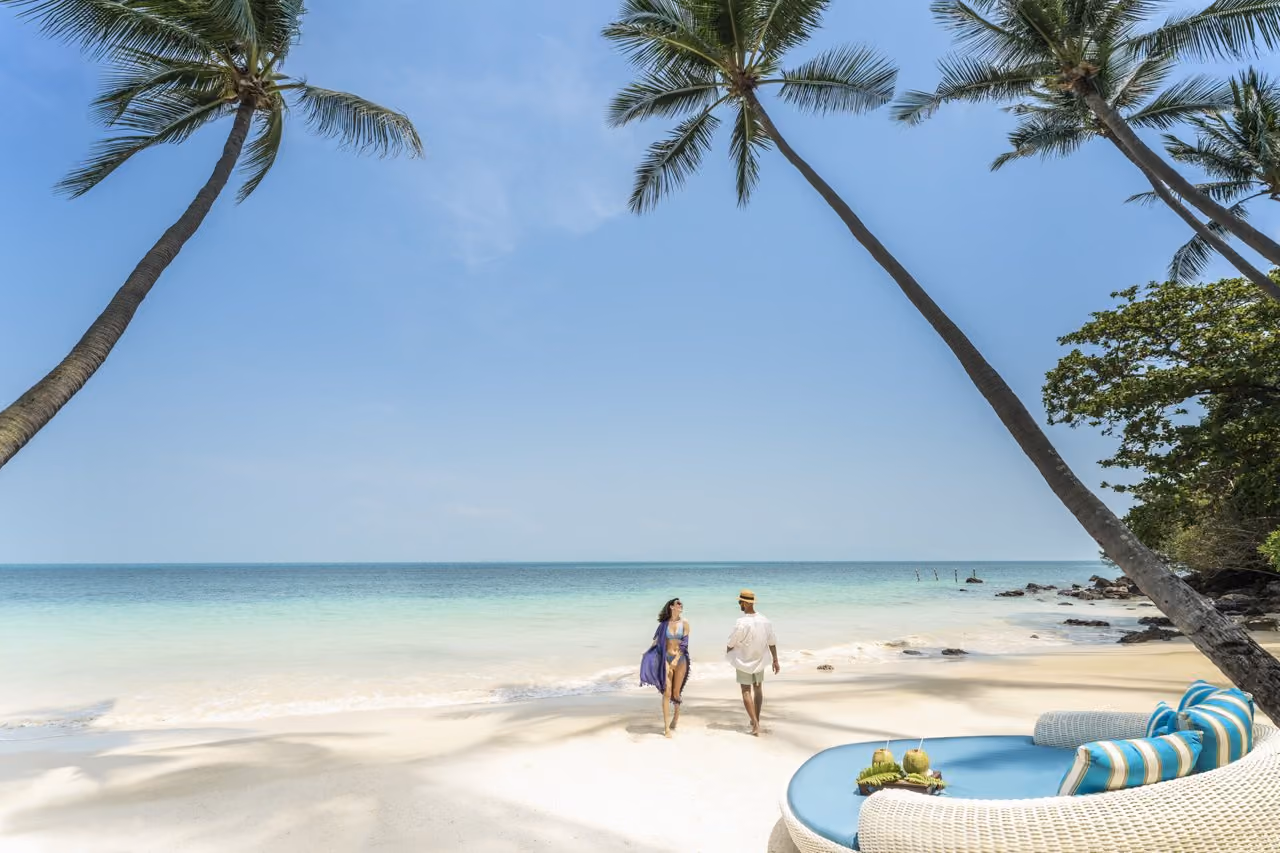 A couple walking on the white-sand beach under leaning palms at Four Seasons Resort Koh Samui