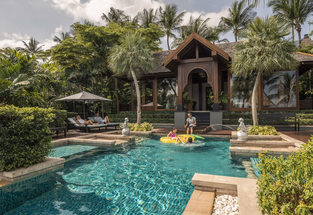 A family in a pool in front of a Thai-style pavilion among palms at Four Seasons Resort Koh Samui