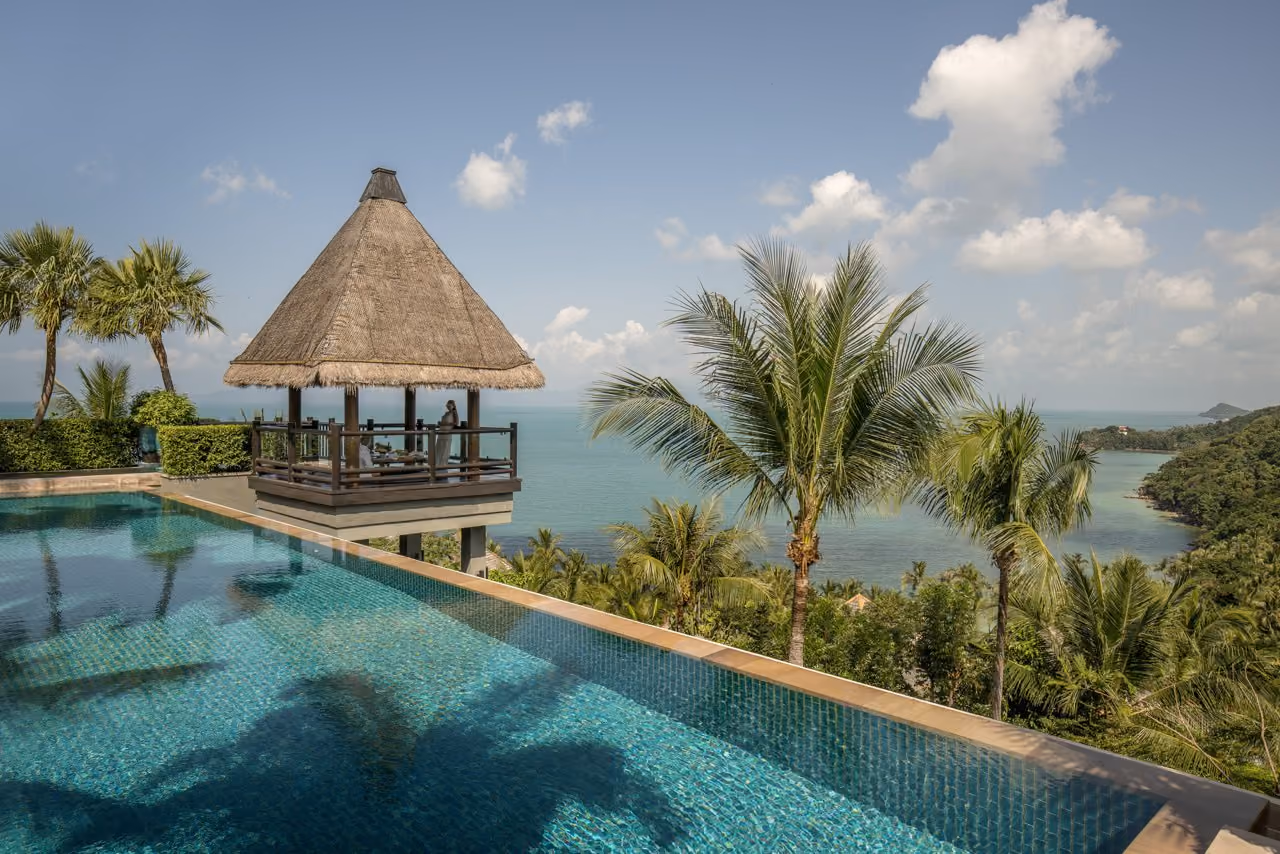 An infinity pool and a thatched sala above the sea and a wooded headland at Four Seasons Resort Koh Samui