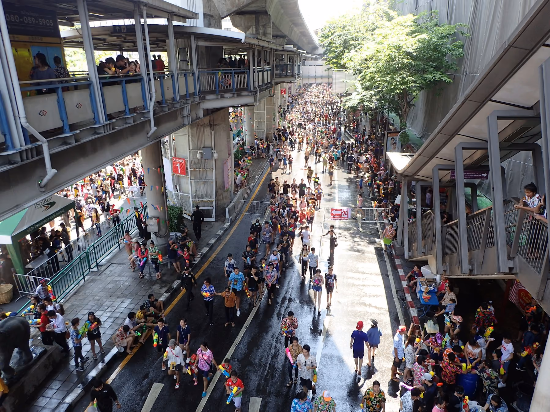 Crowds celebrating Songkran on a wet Bangkok street beneath the skytrain