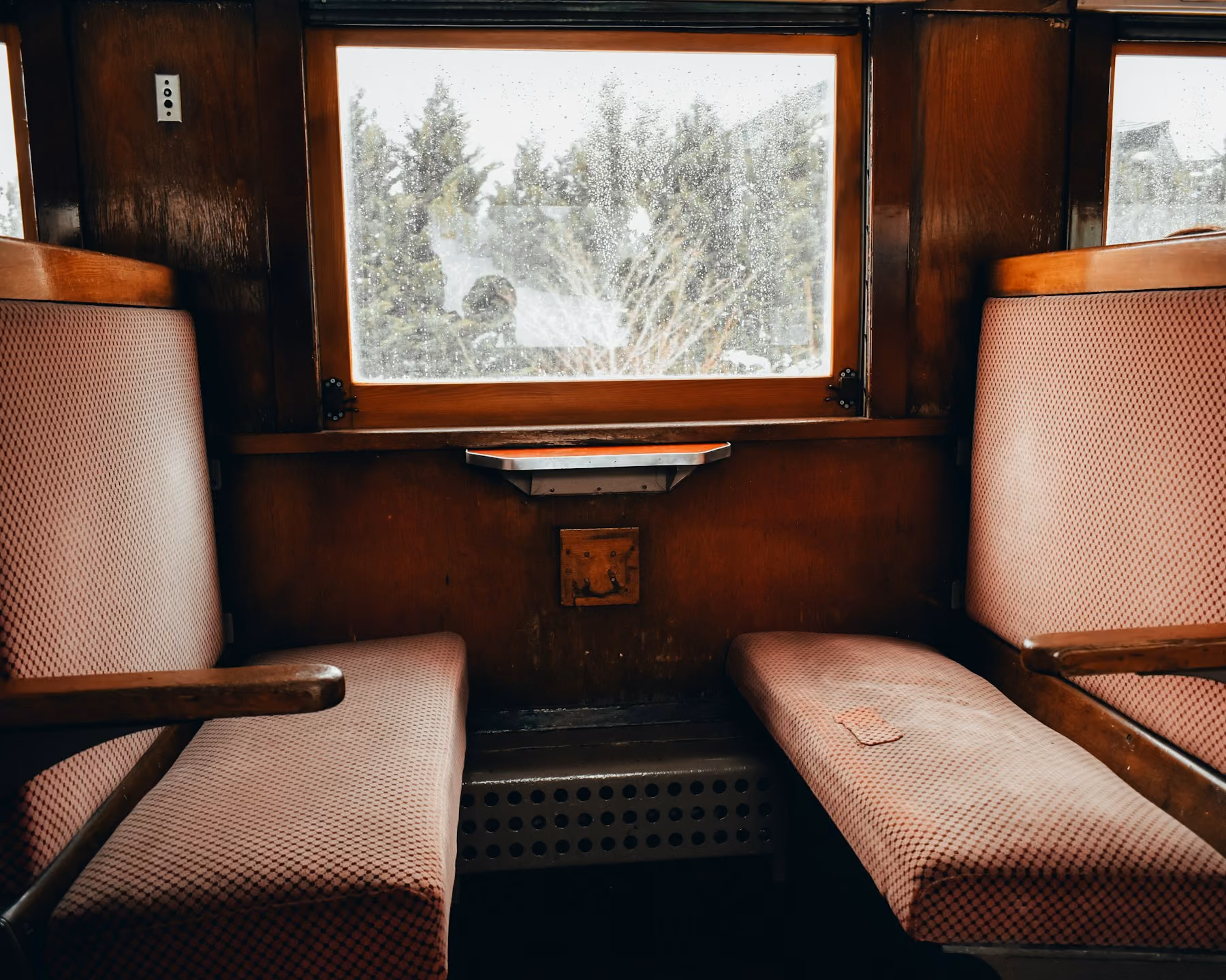 A wood-panelled vintage train compartment with upholstered benches facing a snowy window
