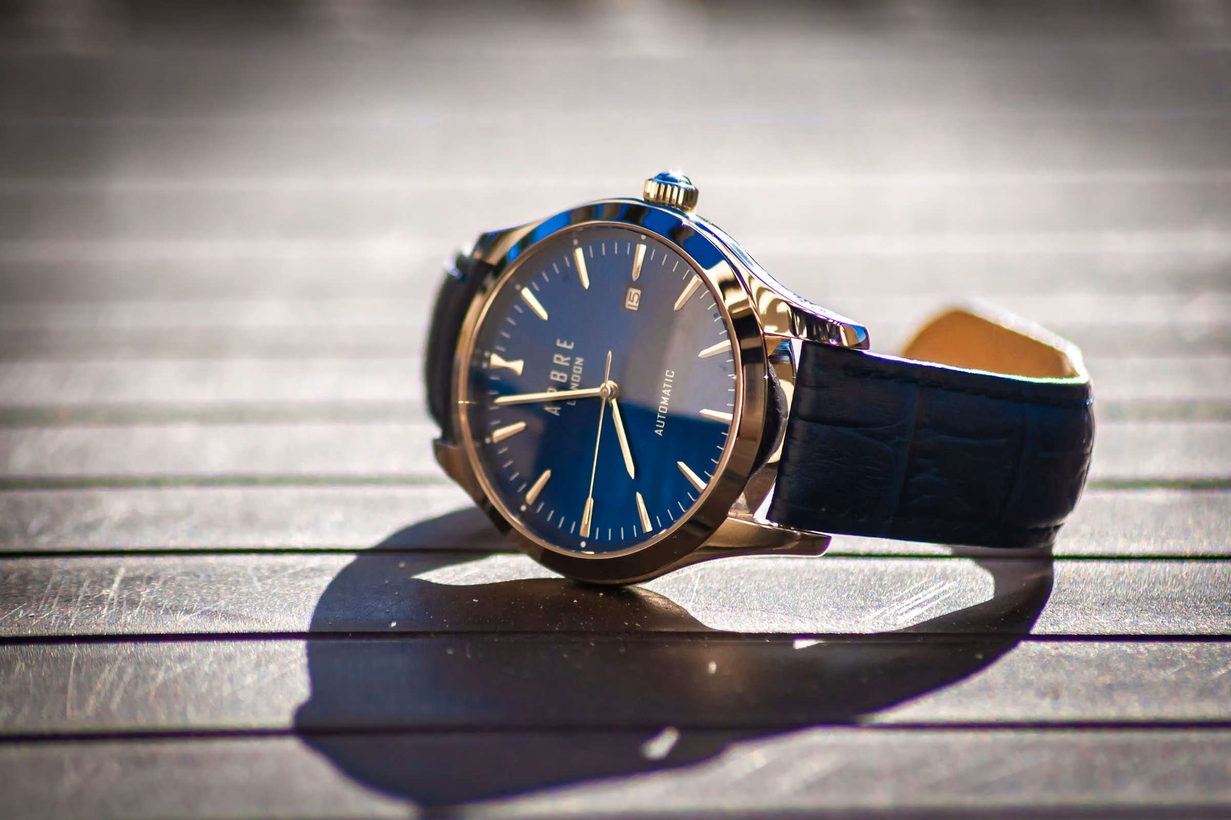 A travel watch with a deep blue dial resting on a sunlit wooden deck