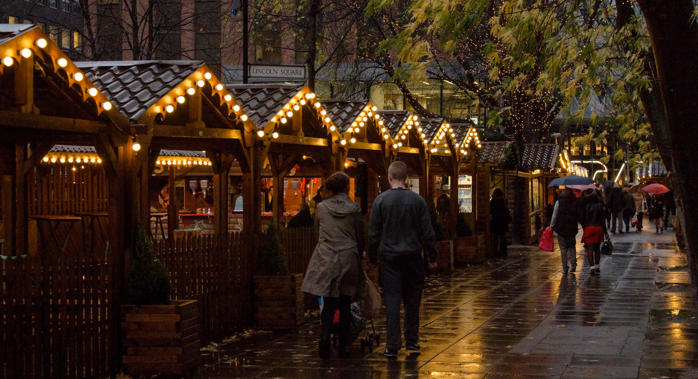 Christmas markets UK: wooden market chalets lit up on a wet winter night