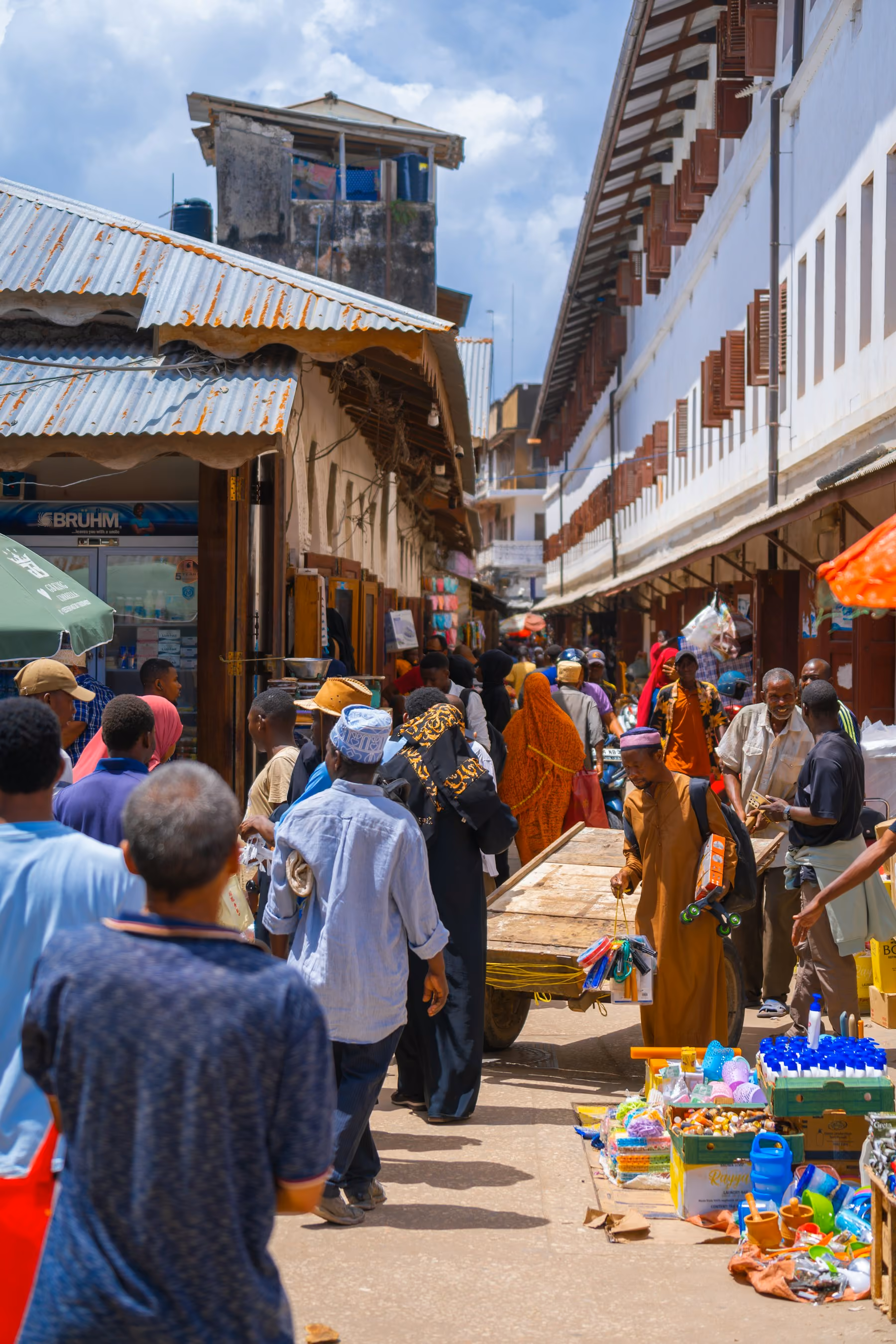 A busy market street beneath carved wooden shutters in Stone Town, Zanzibar